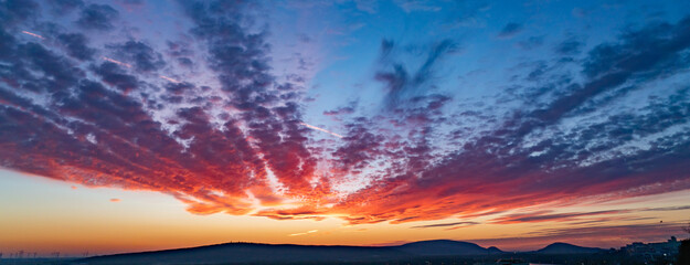 Dramatic sunset sky banner with converging clouds above dark horizon