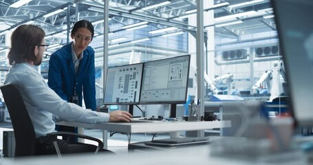 Portrait of a Young Male Engineer and a Asian Team Leader Collaborating on a Project, Using Computer and Talking in a Factory with Equipment Producing Modern Technical Devices for Tech Industries