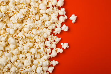 Popcorn scattered on a red background.  A classic movie theater snack. View from above.
