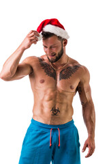 Christmas season: muscular bodybuilder shirtless wearing Santa Claus red hat, isolated on white