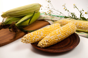 Clay plate with two cobs sweet corn on white wooden background..