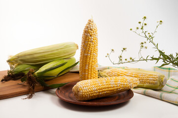Clay plate with two cobs sweet corn on white wooden background..