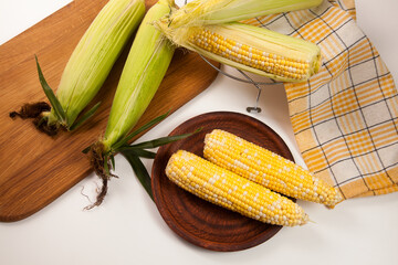 Clay plate with several cobs sweet corn on white wooden background..