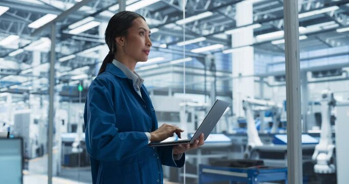 Portrait of a Beautiful Electronics Manufacturing Technician Working on a Laptop Computer at a Factory. Asian Female Specialist Developing, Maintaining, Setting Up Programs for Machine Production