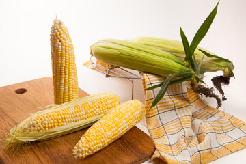 Cutting board with three cobs sweet corn on white wooden background..