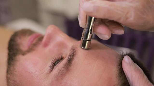 Cosmetic face care. Young handsome man in salon. Dermatological diamond skin cleansing. Close up.