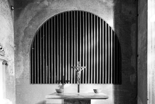 Black and white photo of crucifix on a table inside medieval chapel in Italy