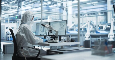 Modern Factory: Industrial Engineer Working on Desktop Computer in Clean Sterile Coveralls. Scientist Using a Microscope, Developing Advanced Solutions for High-Tech Medical Vaccine and Gene Research - Powered by Adobe