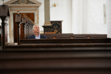 Senior man, sitting and church for religion, faith or pray at cathedral or holy grounds in Jesus Christ. Mature or religious male person looking up in sanctuary for salvation, forgiveness or worship - obrazy, fototapety, plakaty