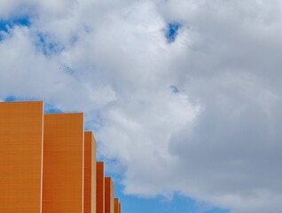 Upward view on buildings corner of vivid orange colour against the blue moody sky with clouds in...