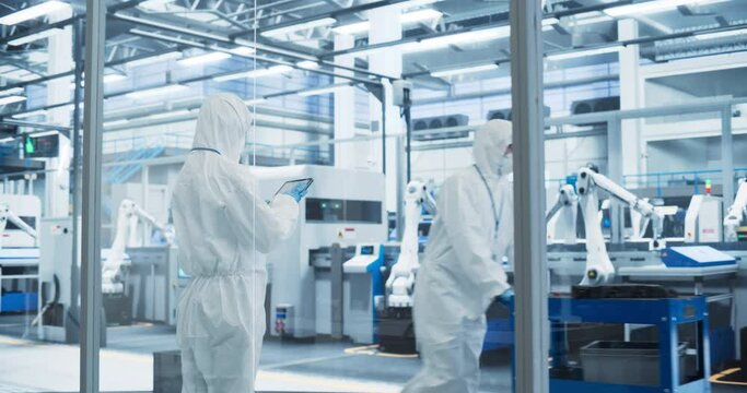 Industrial Scientist Wearing Disposable Protective Suit to Be Protected From Chemical and Biological Dangers. Female Using Tablet Computer, Monitoring Production Process at a Biotechnology Plant
