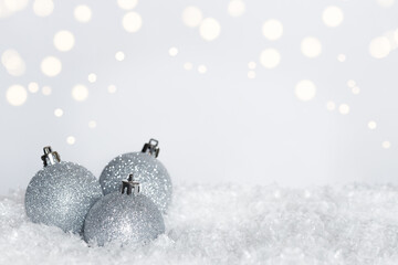 Three silver glitter Christmas ornaments with silver cap on top on bed of snow on blurred white...