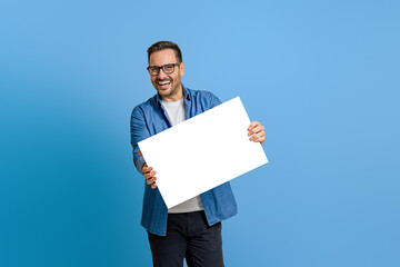 Portrait of cheerful marketing manager showing blank white banner while standing on blue background