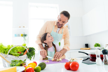 Photo of positive dreamy dad small daughter chopping knife vegetables preparing dinner together indoors home kitchen