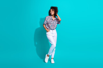Fototapeta na wymiar Full length photo of cheerful gorgeous girl dressed trendy clothes hand touch curly hairdo empty space isolated on cyan color background