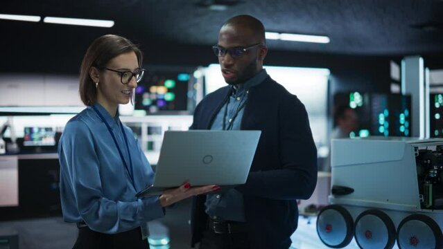 Colleagues Analysing Data Using Laptop Computer and Brainstorming for a Project: Portrait of a Team of Two Engineers Collaborating on Developing a Robot for Deliveries in a Manufacturing Facility