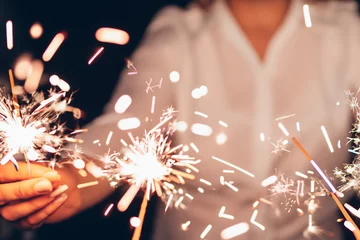 Fotobehang Close up of a hands holding some sparklers celebrating the new year © HarisZai-Designs
