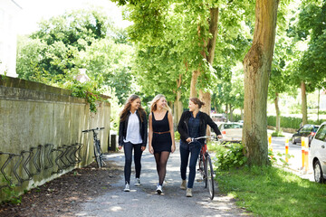Bicycle, friends and happy women walking at school together for education in university. Bike,...