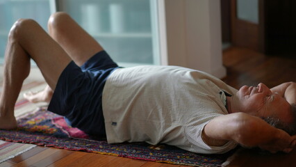 Senior man stretching body in the morning. Eldery caucasian person laid on floor exercising,...