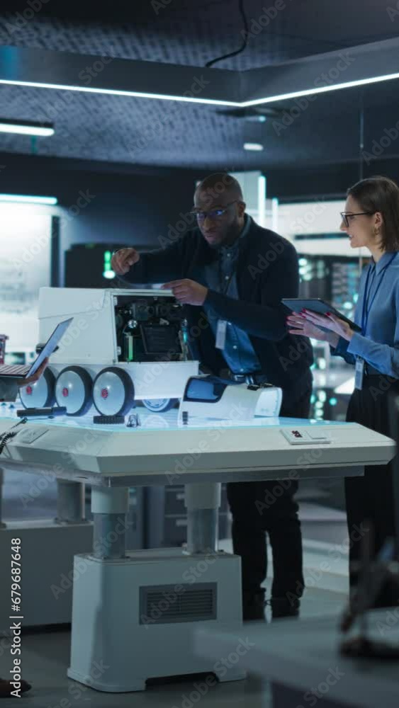 Poster Vertical Screen: Industrial Robotics Specialists Working on a Mobile Robot, Using Tablet and Laptop. Black Male Engineer Discussing an Automated AI Robotic Delivery Assistant with His Young Team