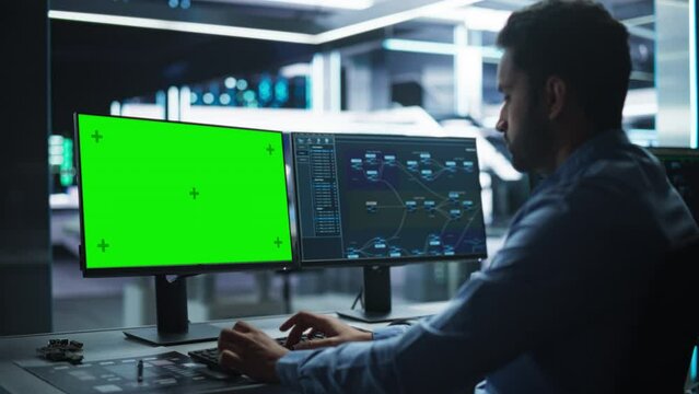 Professional Male IT Technical Support Specialist and Software Developer Working on Computer with Green Screen Mock-display in Monitoring Control Room. Programmer Fixing Hiccups in Service