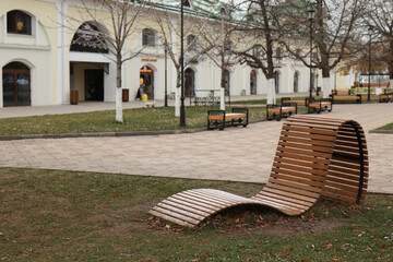 A wooden chaise longue in a park near the stavrine building of a shopping row in the city of Ryazan