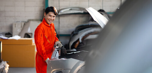 Asian thai male car repair worker taking off car bumper part to get it repaired. male mechanic repairs car in garage. Car maintenance and auto service garage concept