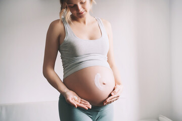 Pregnant woman applying moisturizer cream on her belly. Body skin care during pregnancy.