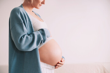 Beautiful pregnant woman hugging her belly in white background. Expectant mother waiting for baby birth during pregnancy. Concept of maternal health, visiting doctor and gynecological checkup. - obrazy, fototapety, plakaty