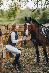 Obraz premium A young female equestrian stands near her horse and prepares for a competition.