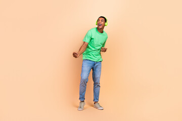 Fototapeta premium Full length photo of positive man wear stylish t-shirt jeans in headphones dancing look empty space isolated on beige color background