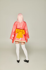 back view of anime style woman in blonde wig and short pink kimono with white knee socks on grey