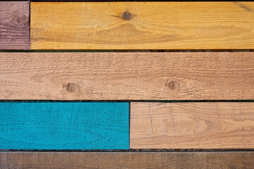 Fragment of a wall made of multi-colored rough untreated wooden boards. Blue, yellow and natural wood color. Background. Texture. Form.