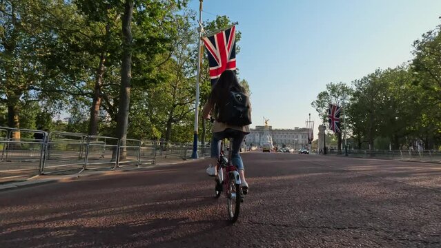 Tracking shot of young tourist woman riding bicycle towards Buckingham palace London City of Westminster on a beautiful sunny day