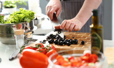 Male Hands Chopping Round Black Olives Slices. Chef Cutting Fresh Vegetable Ingredient on Wooden...