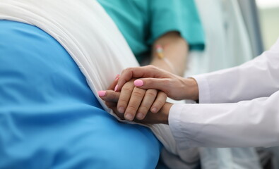 Close-up of people holding hands of each other. Woman calming to sick patient in hospital ward. Doc...