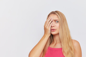 Obraz premium Young woman with long fair hair poses on white backdrop with one hand covering half of her beautiful face, hard day concept, copy space