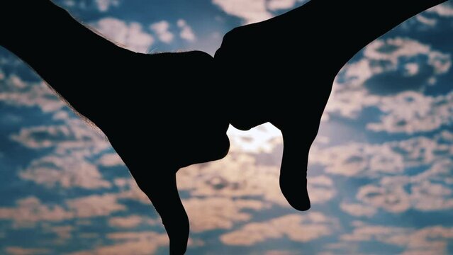 Close up view: silhouettes of persons are showing two thumbs down hand gestures against the cloudy sunset, sunrise blue sky with sun lens flares. Disapproval, negative and decline concept