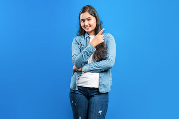 Isolated on blue background an attractive Indian girl indicating fore finger to the side for...