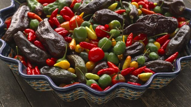 Different varieties of chilies on a plate. Ripe and unripe Brazilian Red Olive, Peruvian Machu Picchu tabasco, and biquinho yellow. Table spin. 