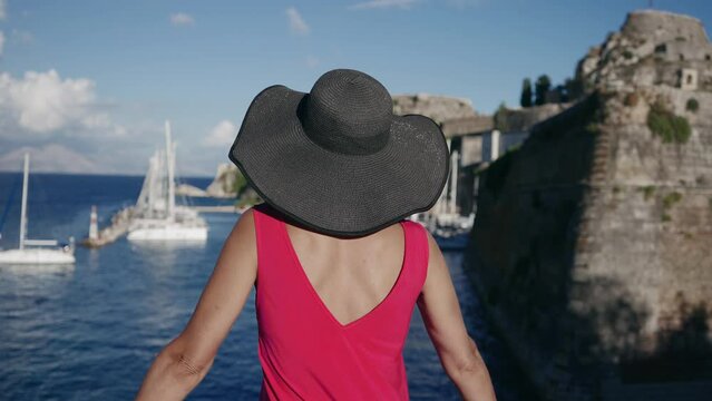 Tourist woman in dred dress enjoy view of the old Venetian fortress and yachts pier of Corfu Island town, Greece