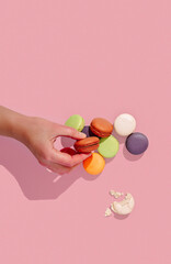 french dessert macarons, lying in a pile, different colors on a textureless pink background, hand with macaron, top view,