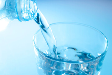 Pour water from a bottle into a clear glass. Image in blue tones.