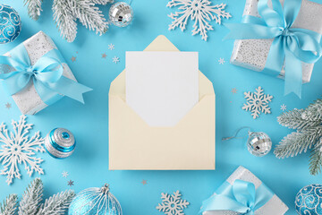 It's time to write a list for Santa Claus and share your biggest wishes. Top view shot of beige envelope with card, frosty fir twigs, presents, xmas balls, snowflakes, stars on blue background