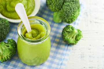 Green broccoli baby food in white bowl and jar on table. Green baby food. Child first feeding...