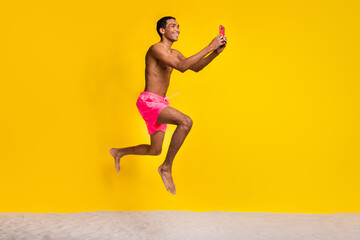 Fototapeta na wymiar Full length photo of pretty positive shirtless man jumping high texting instagram twitter telegram facebook isolated yellow color background