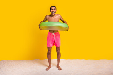 Full length photo of positive excited masculine guy enjoying swimming inflatable circle isolated yellow color background - obrazy, fototapety, plakaty