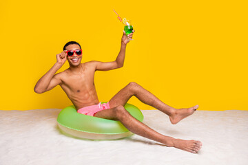 Full length photo of attractive excited shirtless man sitting inflatable circle rising cocktail...
