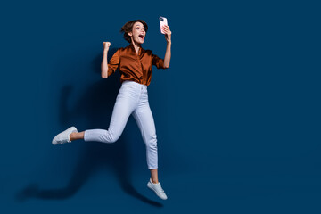 Full length photo of lucky funky lady wear brown shirt jumping winning game modern device empty space isolated blue color background
