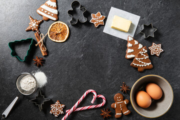 christmas, food cooking and winter holidays concept - close up of iced gingerbread cookies, molds, flour and other ingredients on black table top at kitchen - Powered by Adobe